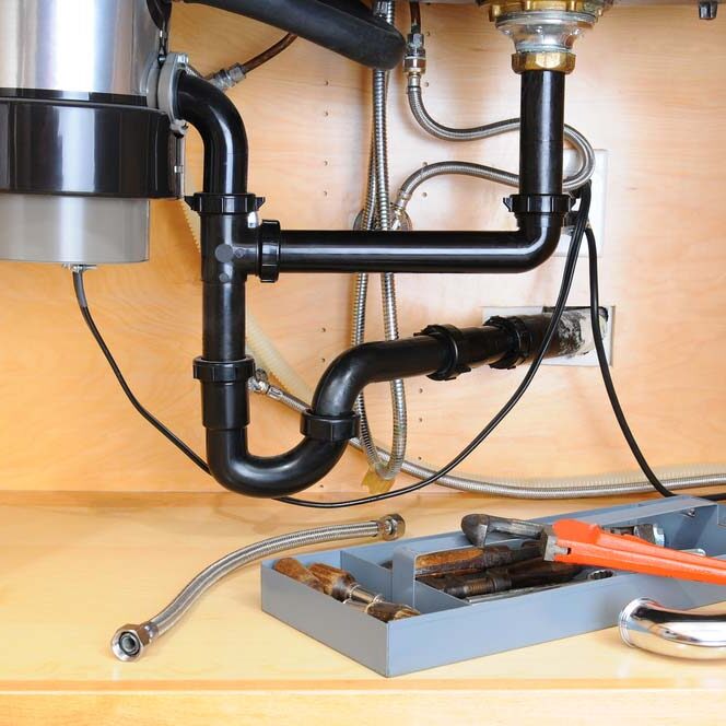 Detail of the plumbing system under a modern kitchen sink, with a plumbers tool tray and equipment. Horizontal format.