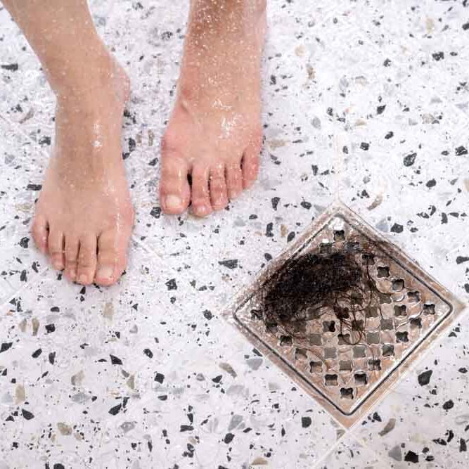 A woman suffering from alopecia is taking a shower, there is hair in the drain next to her feet